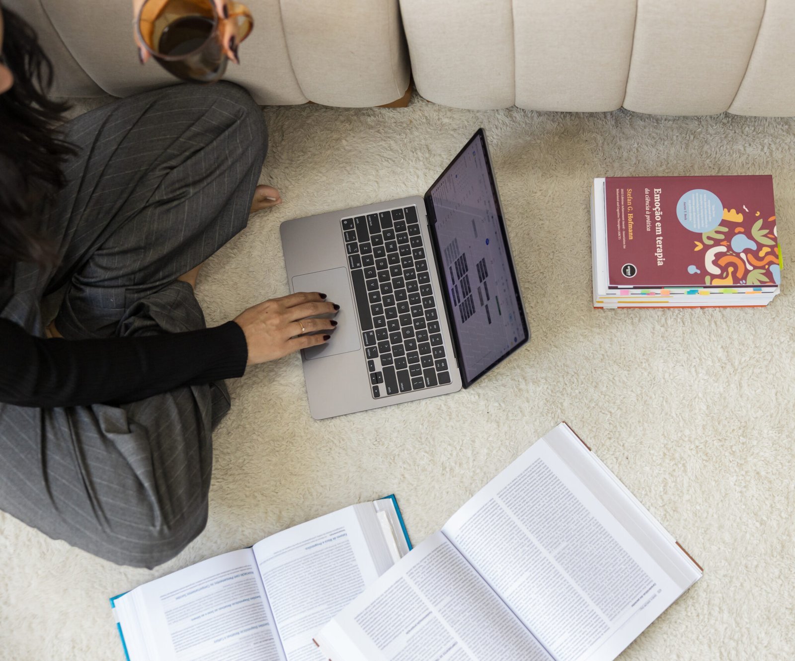 Pessoa estudando com notebook e livros abertos sobre um tapete.